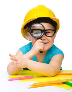 Child in a hard hat looking through a magnifying glass