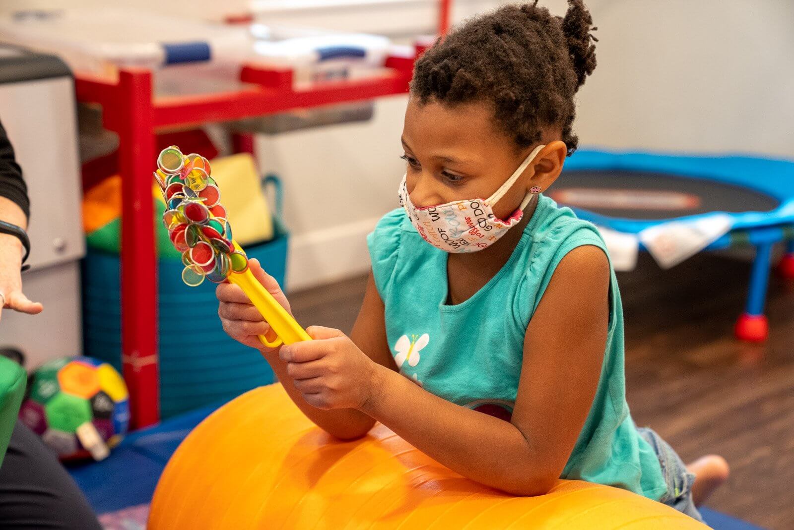 Girl in a face mask playing with a toy on a therapy ball