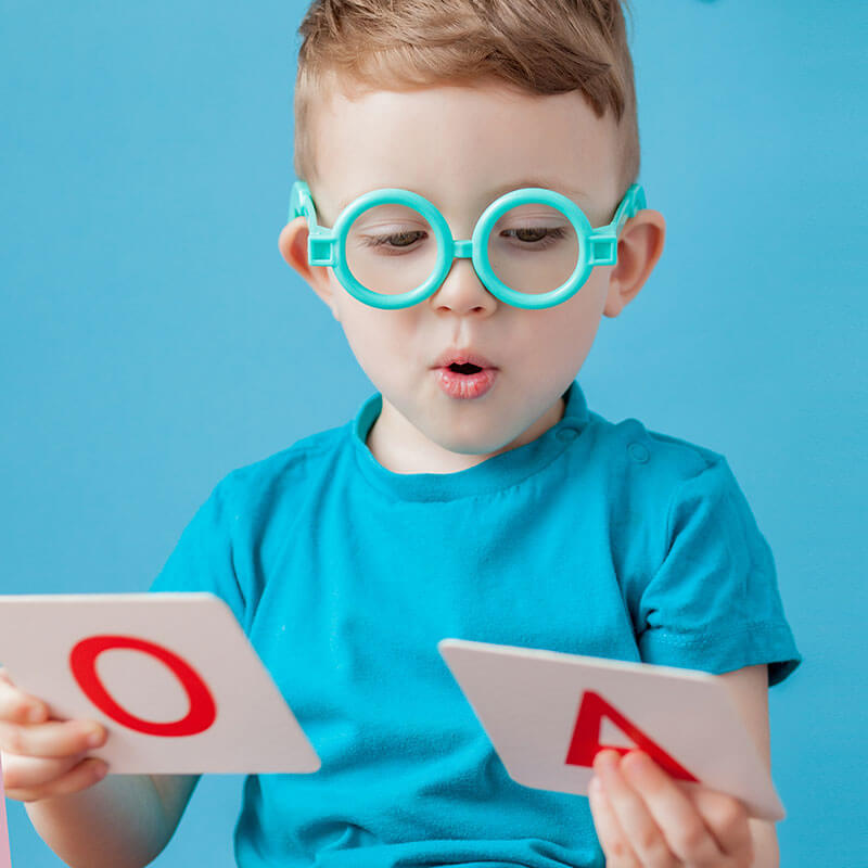 Speech therapy: a young boy in glasses holding letter cards