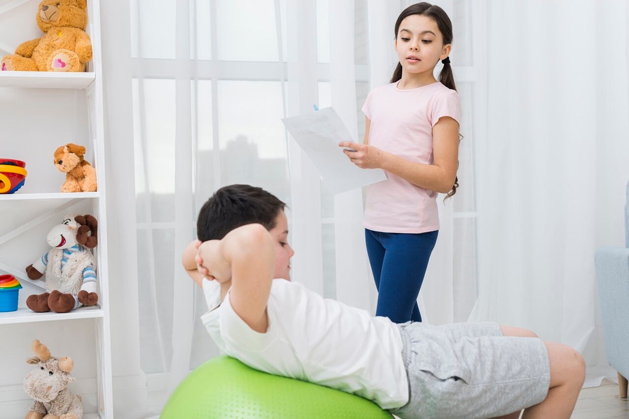 Girl watching a boy exercise on a therapy ball