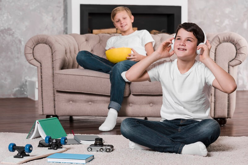 Two boys relaxing in a living room, one wearing headphones