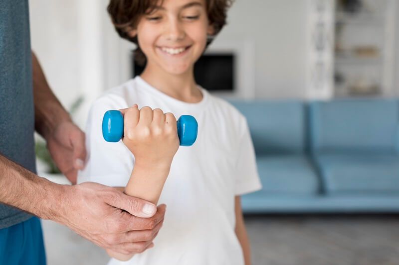 Child lifting a small dumbbell with help from a therapist